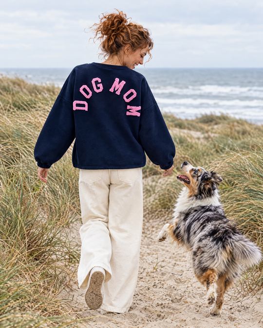 Frau im Dog Mom Sweatshirt in Navy mit rosa Schrift und Australian Shepherd in den Dünen (KI-Bild)